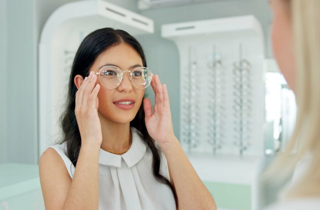 An adult tries on new, white, round frames at their eye doctor's clinic.