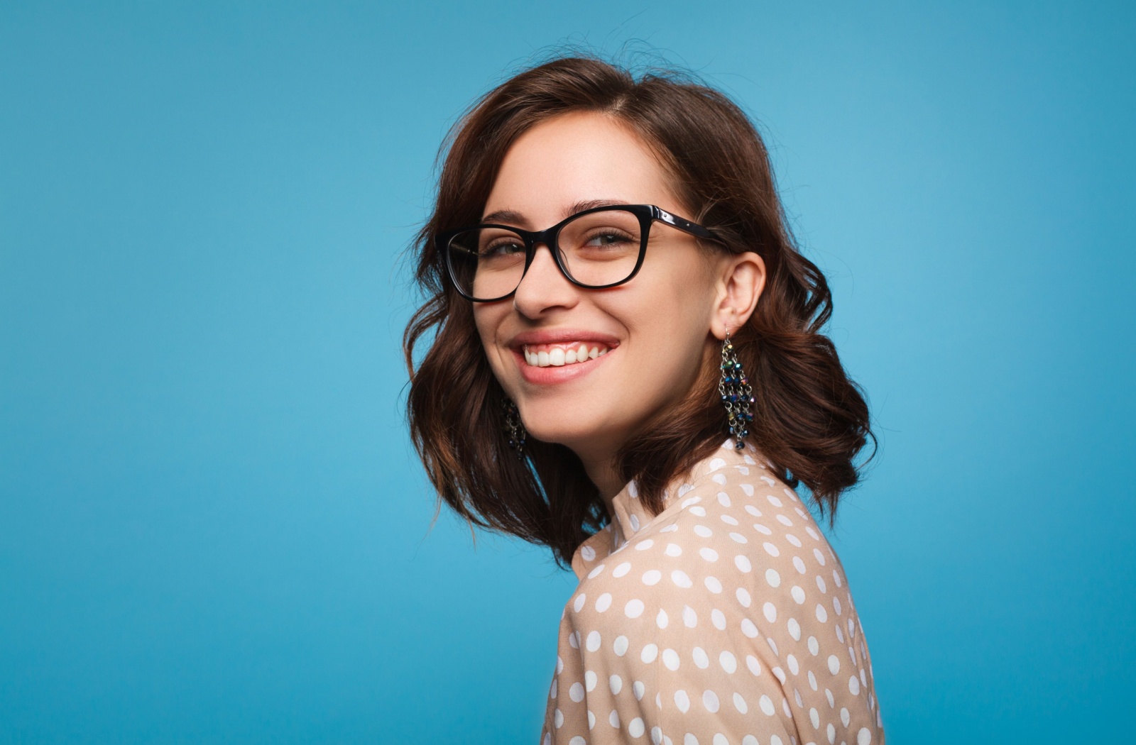 A young woman wearing a stylish pair of glasses smiles over her shoulder.