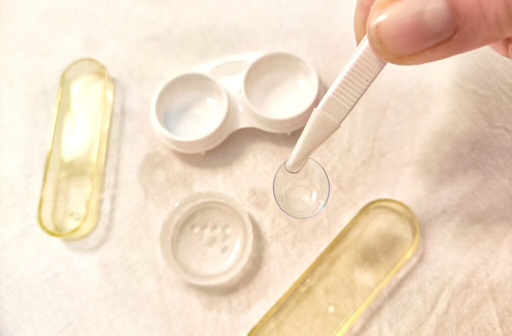 An individual holds a contact lens with tweezers for hygienic reasons while cleaning them in solution