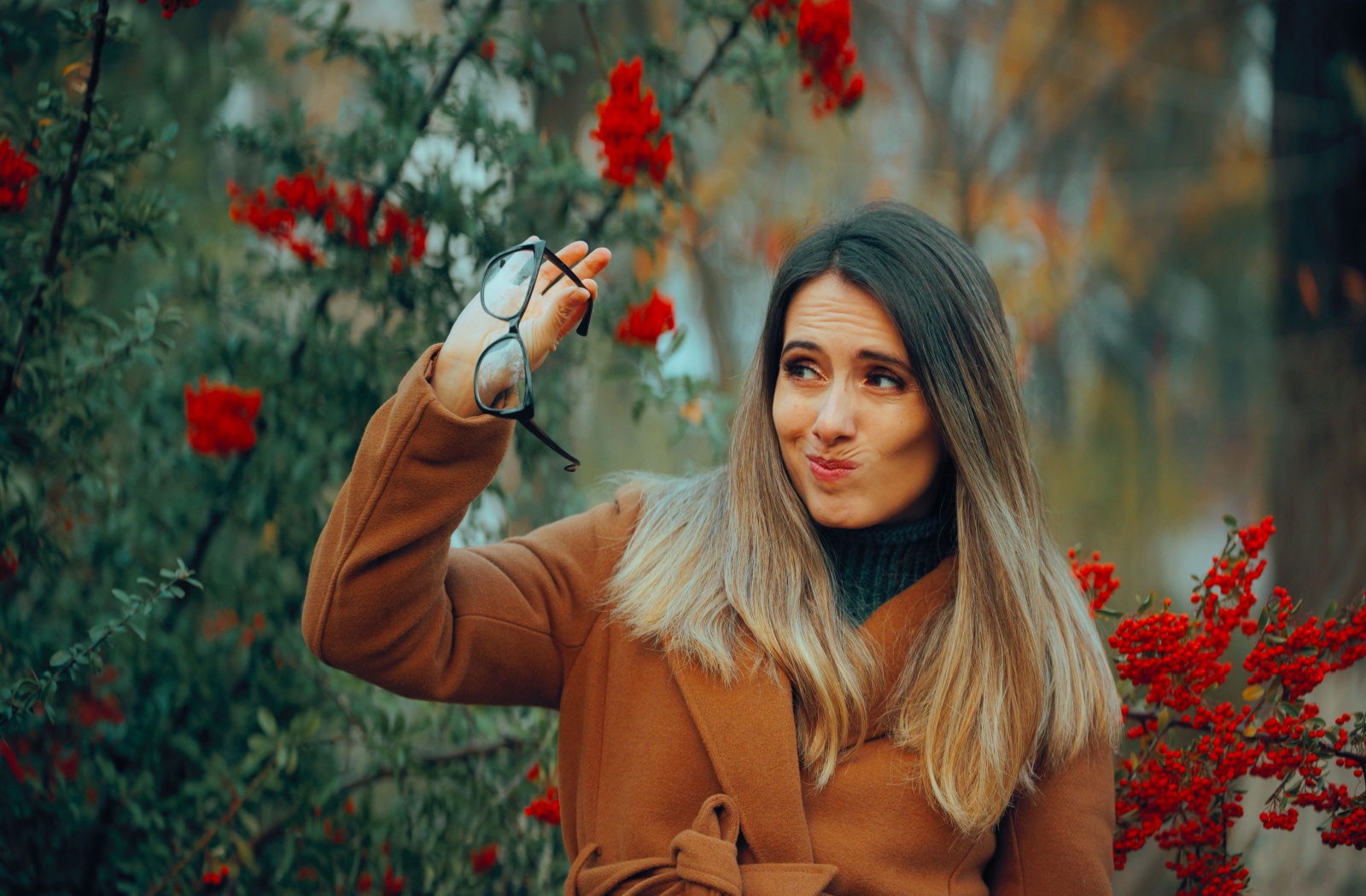 An adult in the outdoors grimaces as they hold their outdated prescription eyeglasses, frustrated that they’re not helping