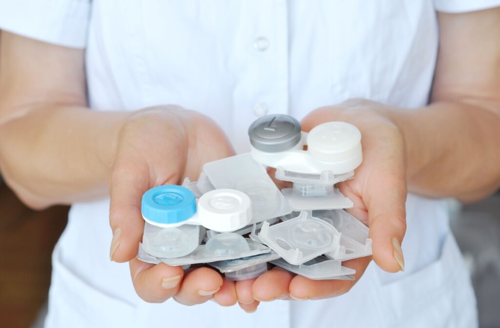 A person holds several contact lens cases in their hands.