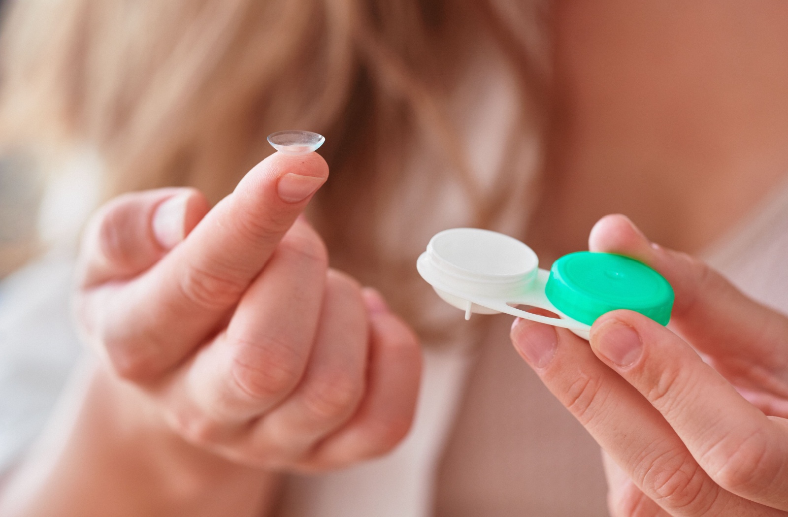 A close-up photo of a person holding a contact lens and a contact lens case.
