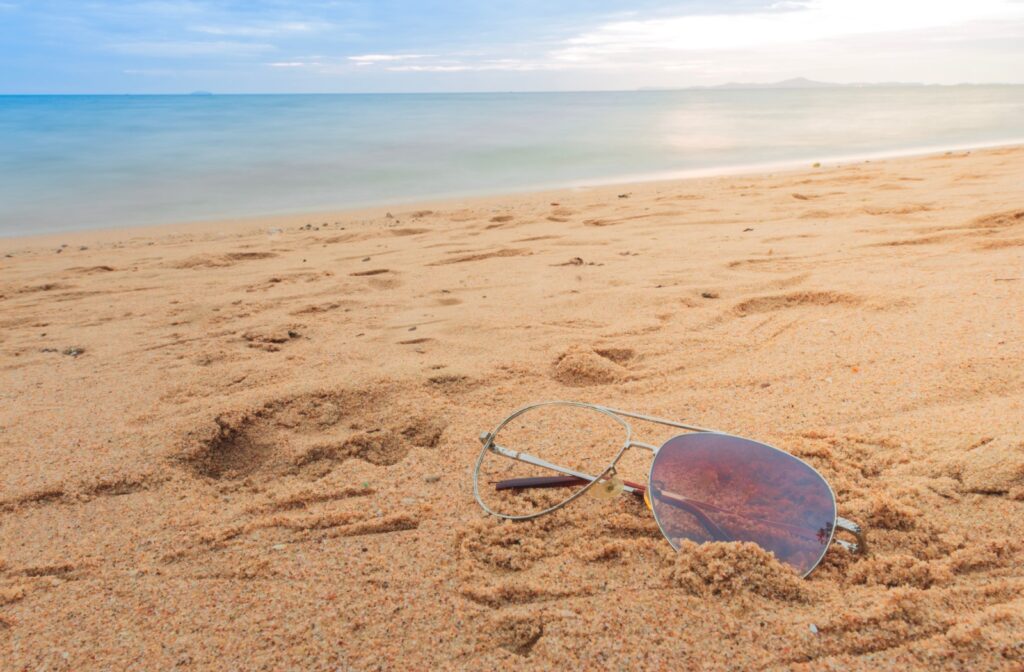A pair of broken sunglasses with a missing lens half buried in the sand.