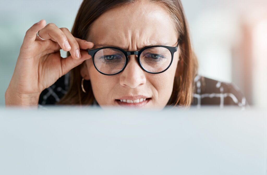 A women holding her glasses closer to her face as she squints at her computer screen