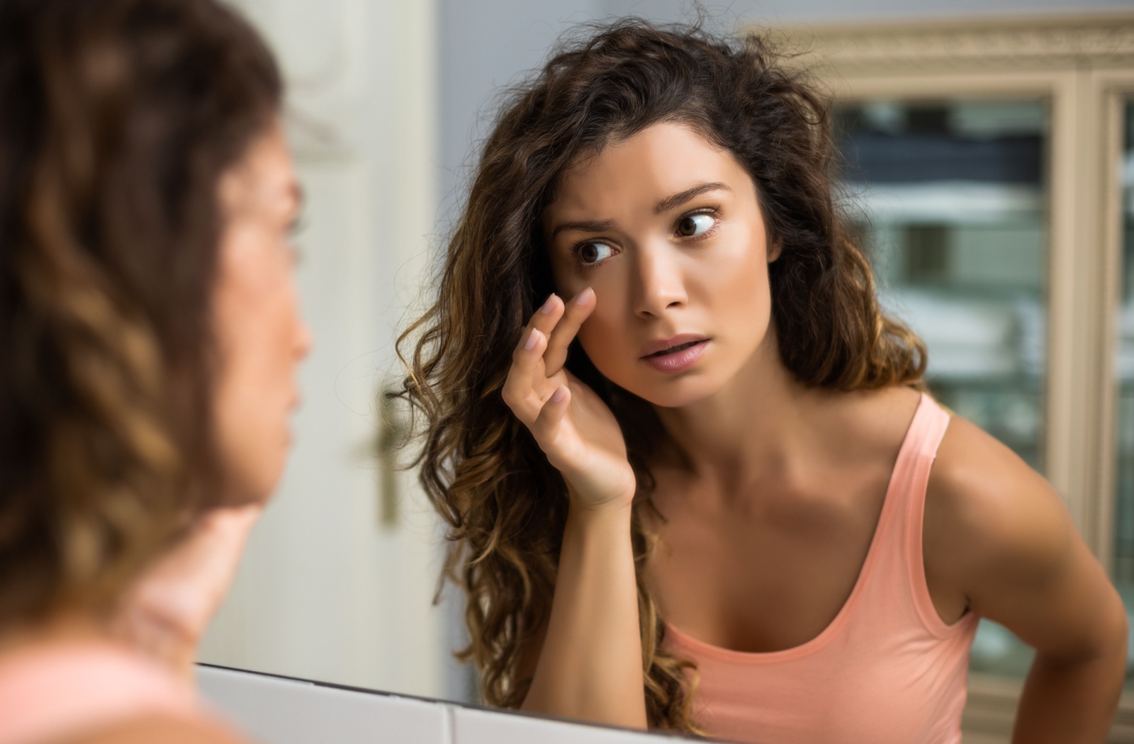 A person looks at their contact lens in their eye using a mirror